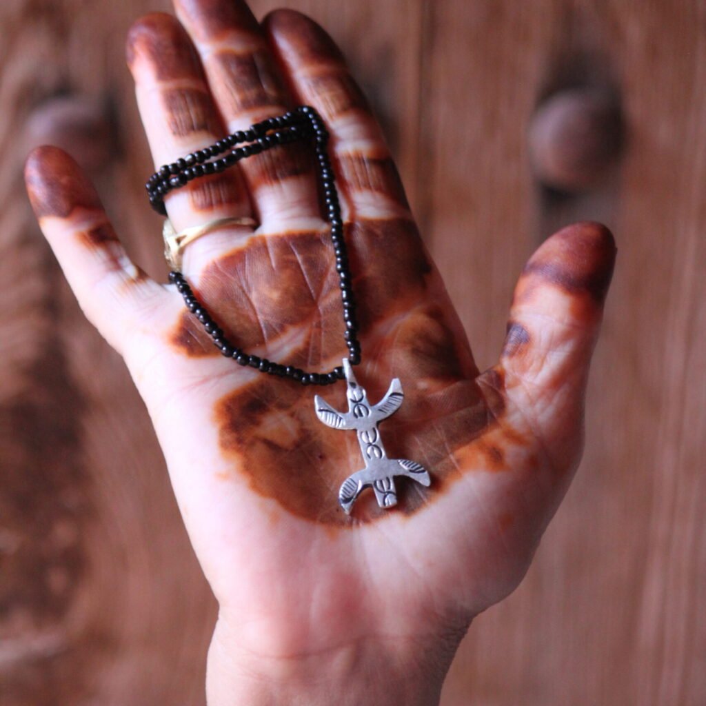 Pendentif amazigh en métal plaqué argent avec motif gravé, monté sur un collier de perles noires.