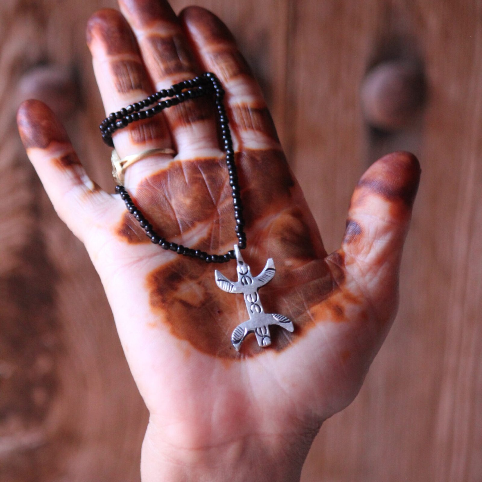 Pendentif amazigh en métal plaqué argent avec motif gravé, monté sur un collier de perles noires.