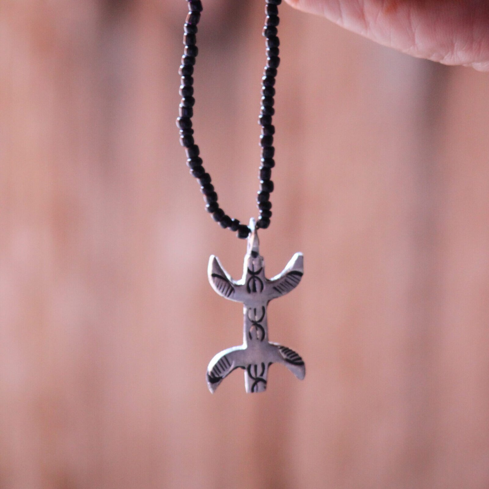 Pendentif amazigh en métal plaqué argent avec motif gravé, monté sur un collier de perles noires.