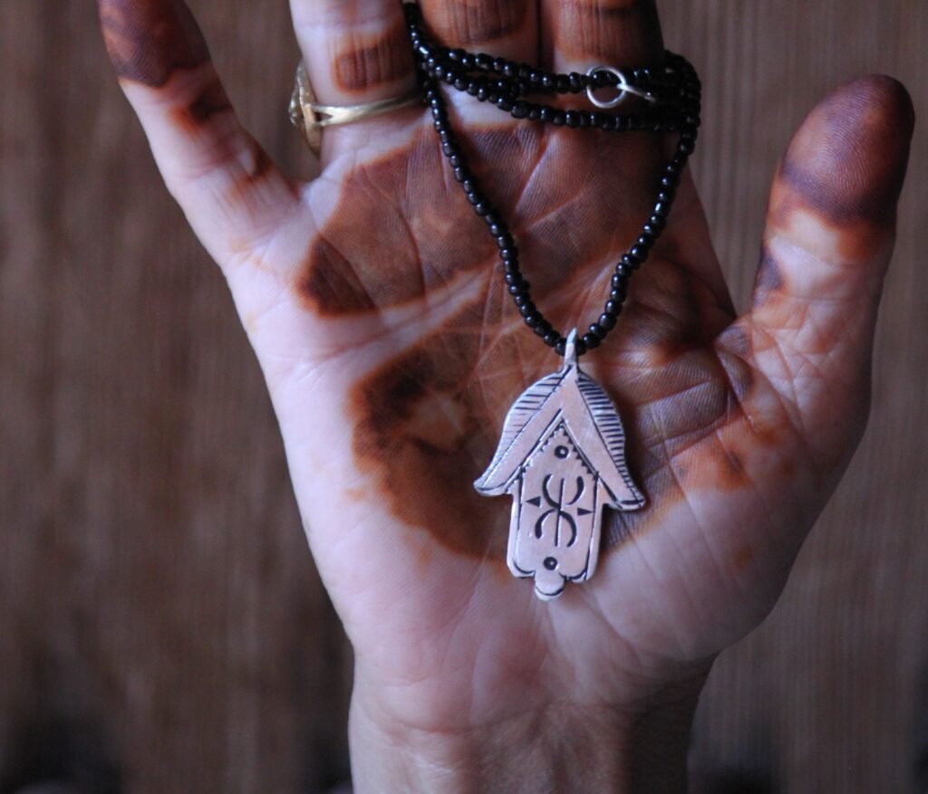 Pendentif amazigh en métal plaqué argent avec motif gravé, monté sur un collier de perles noires.