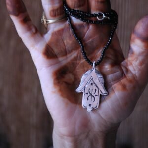 Pendentif amazigh en métal plaqué argent avec motif gravé, monté sur un collier de perles noires.