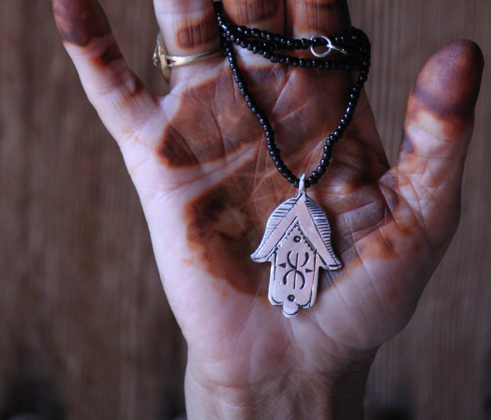 Pendentif amazigh en métal plaqué argent avec motif gravé, monté sur un collier de perles noires.