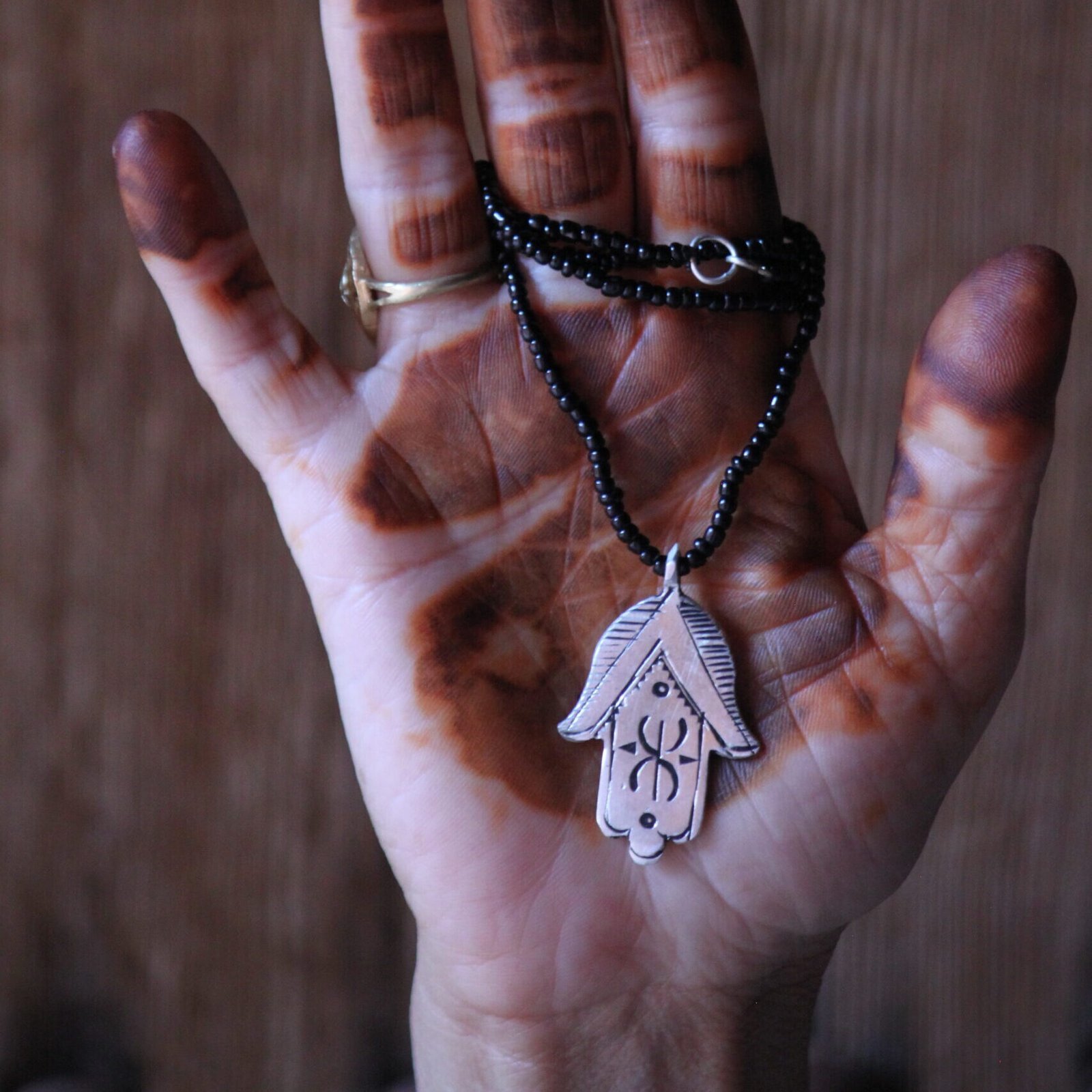 Pendentif amazigh en métal plaqué argent avec motif gravé, monté sur un collier de perles noires.