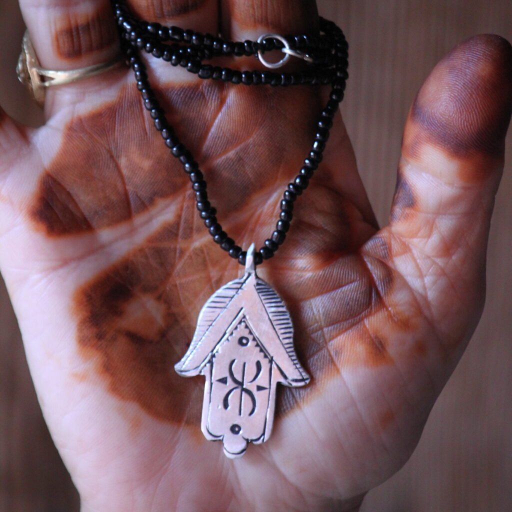 Pendentif amazigh en métal plaqué argent avec motif gravé, monté sur un collier de perles noires.