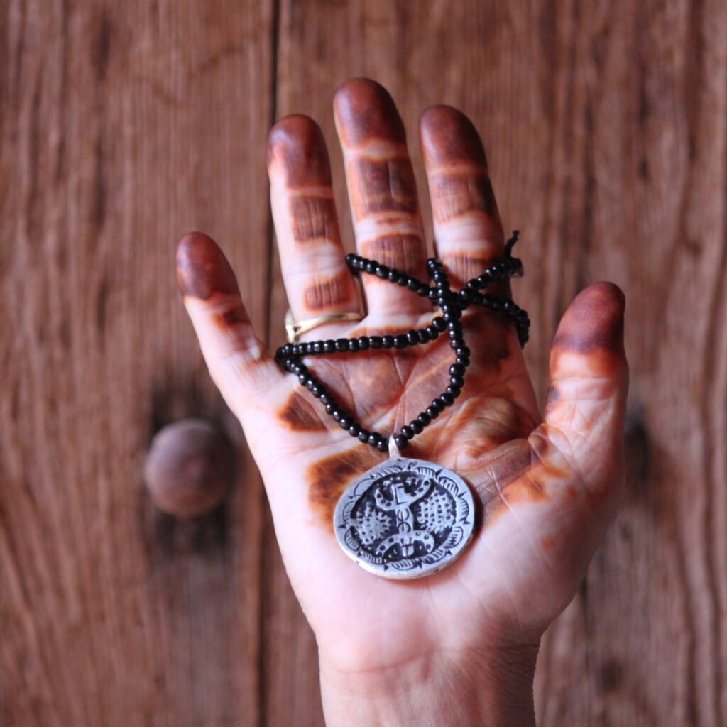 Pendentif amazigh en métal plaqué argent avec motif gravé, monté sur un collier de perles noires.