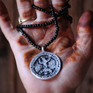 Pendentif amazigh en métal plaqué argent avec motif gravé, monté sur un collier de perles noires.
