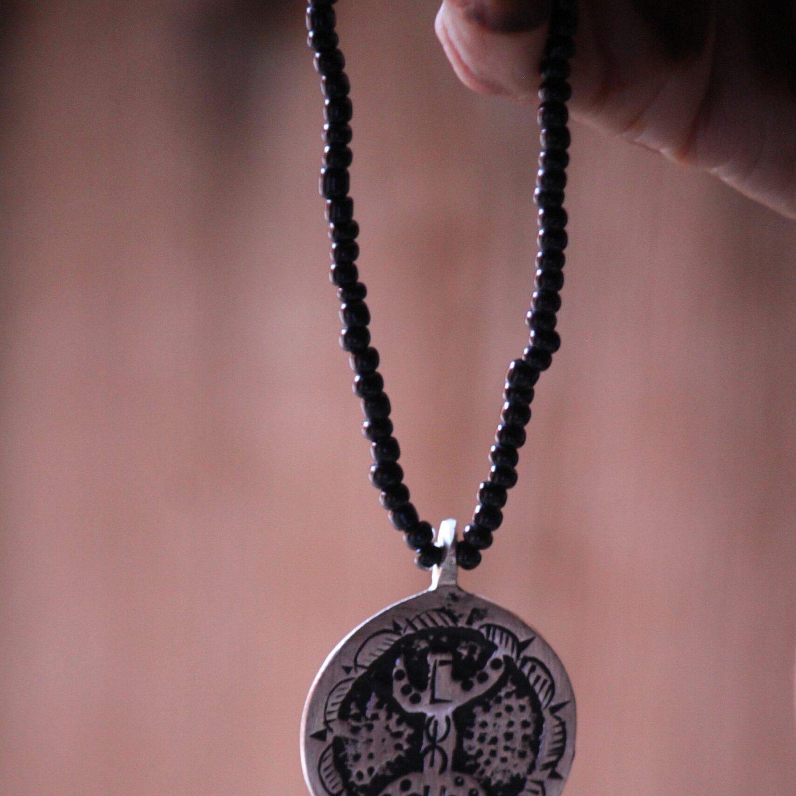 Pendentif amazigh en métal plaqué argent avec motif gravé, monté sur un collier de perles noires.