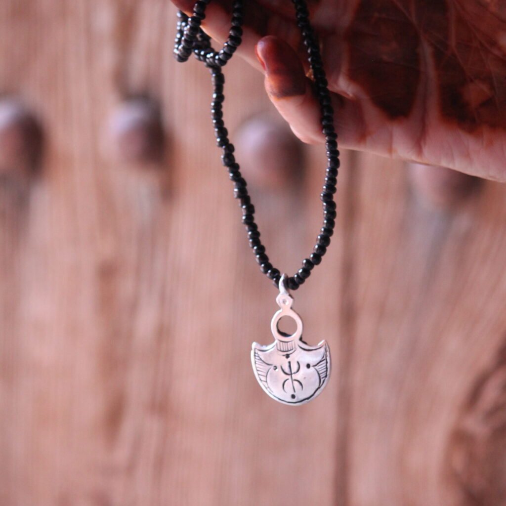 Pendentif amazigh en métal plaqué argent avec motif gravé, monté sur un collier de perles noires.