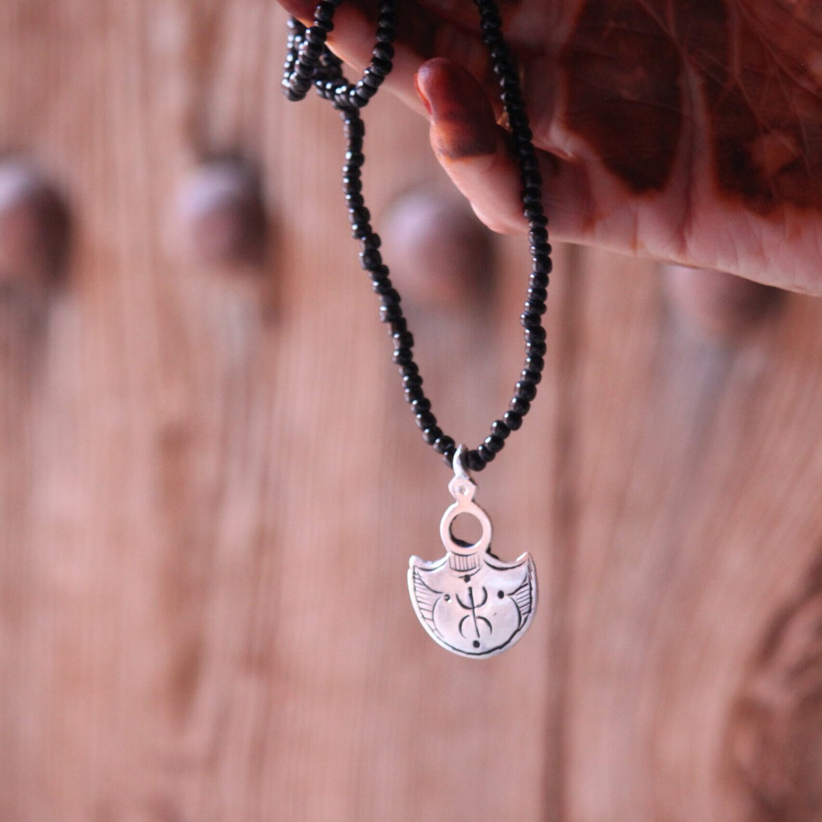 Pendentif amazigh en métal plaqué argent avec motif gravé, monté sur un collier de perles noires.