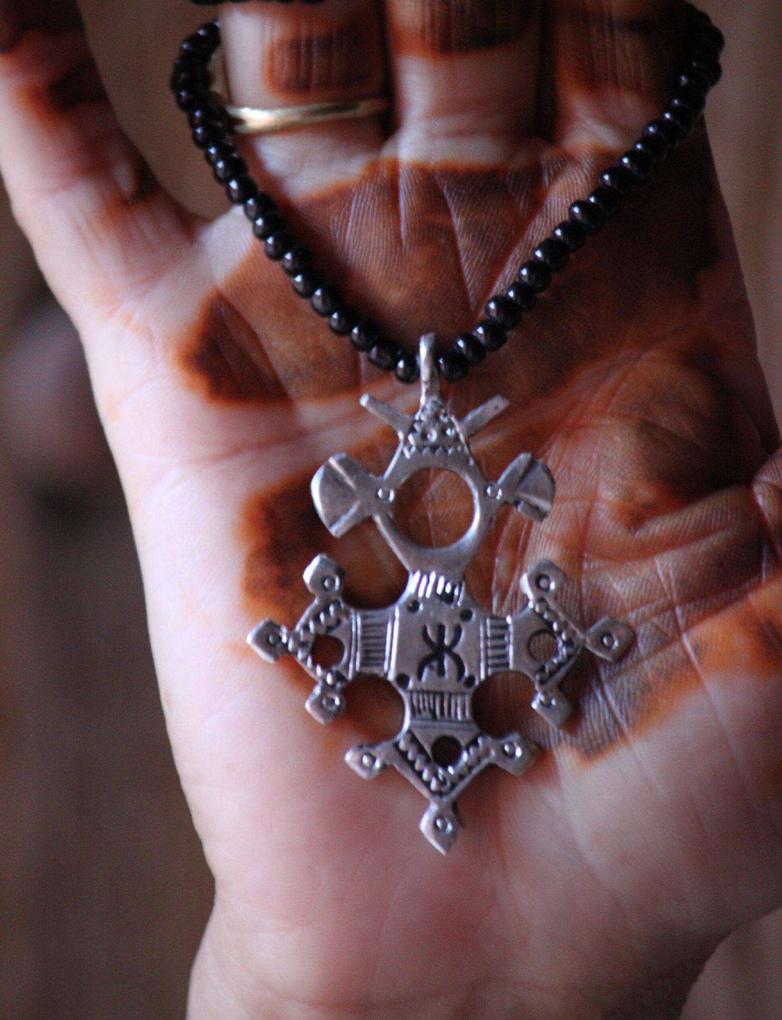 Pendentif amazigh en métal plaqué argent avec motif gravé, monté sur un collier de perles noires.