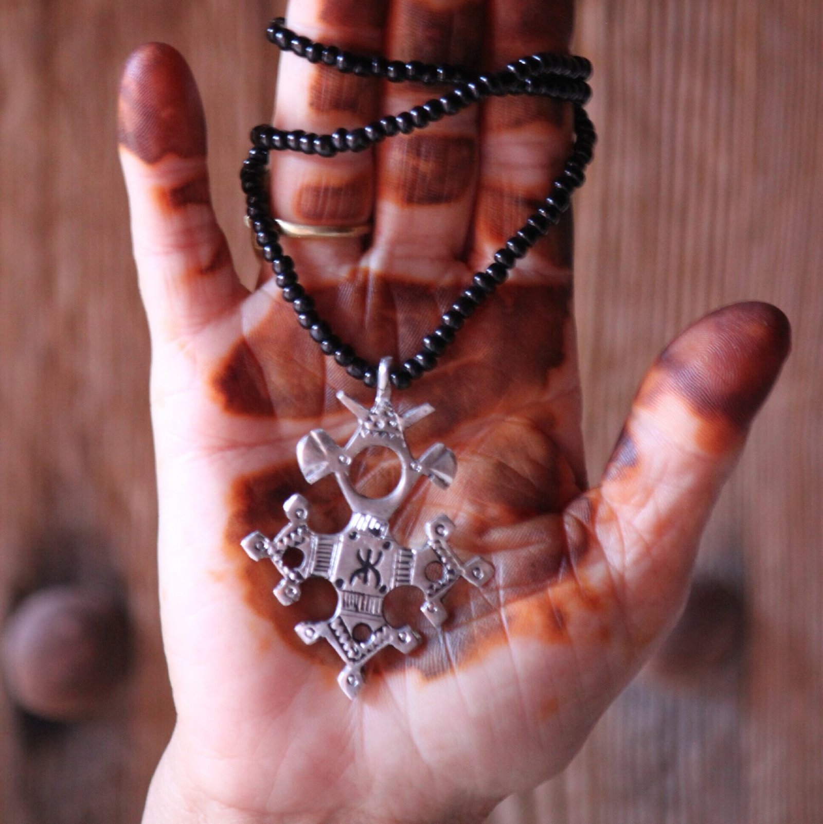 Pendentif amazigh en métal plaqué argent avec motif gravé, monté sur un collier de perles noires.