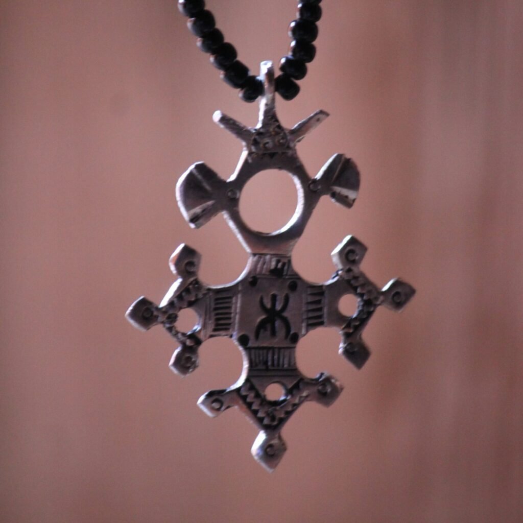 Pendentif amazigh en métal plaqué argent avec motif gravé, monté sur un collier de perles noires.