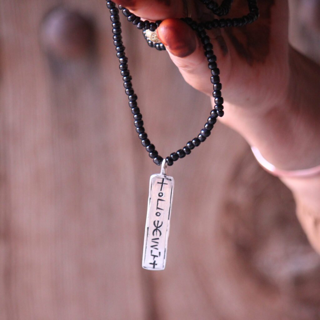 Pendentif amazigh en métal plaqué argent avec motif gravé, monté sur un collier de perles noires.