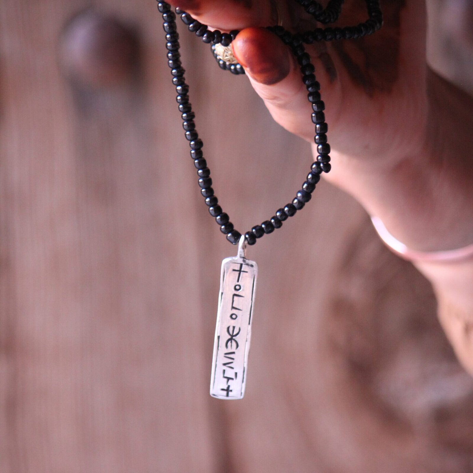 Pendentif amazigh en métal plaqué argent avec motif gravé, monté sur un collier de perles noires.