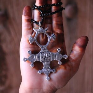 Pendentif amazigh en métal plaqué argent avec motif gravé, monté sur un collier de perles noires.