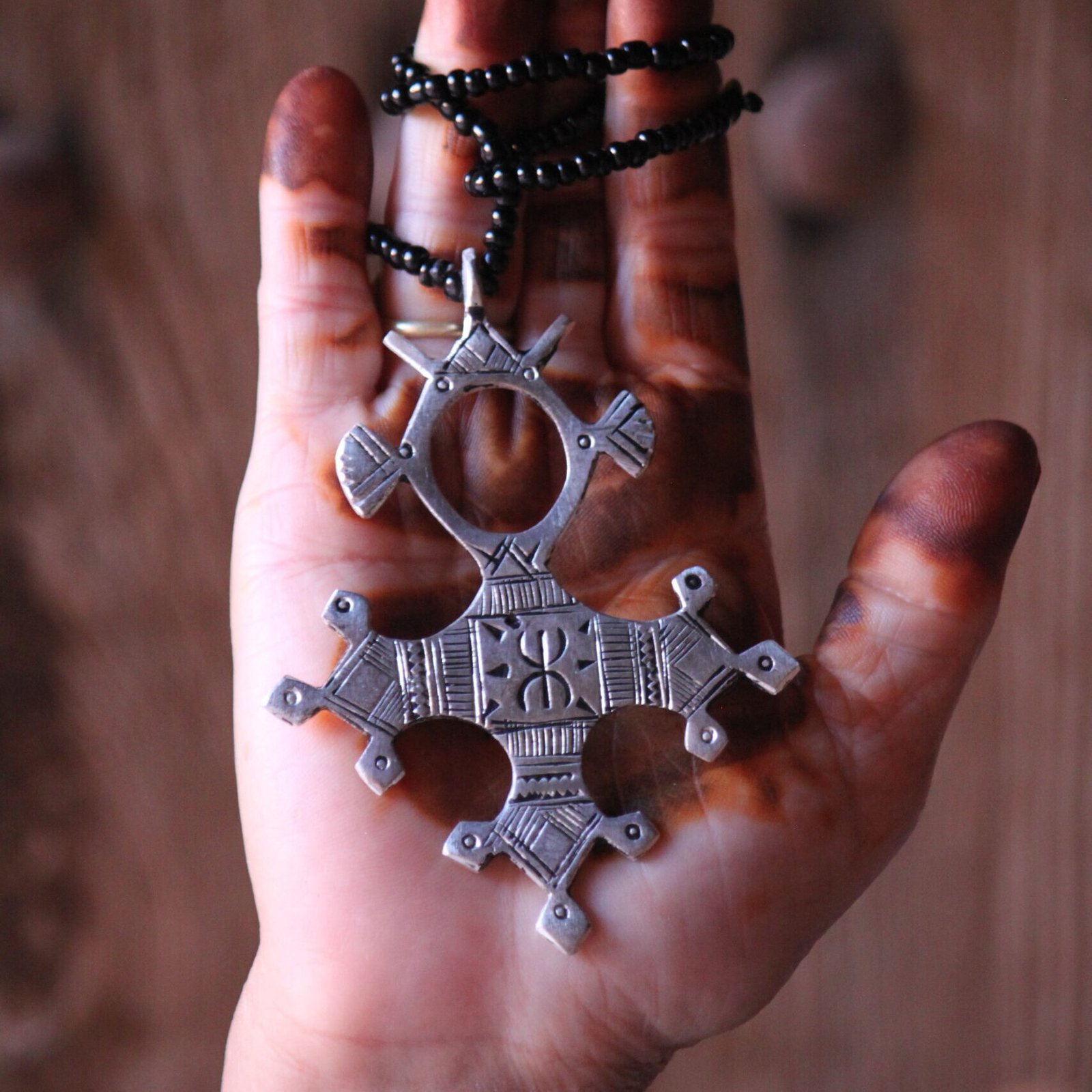 Pendentif amazigh en métal plaqué argent avec motif gravé, monté sur un collier de perles noires.