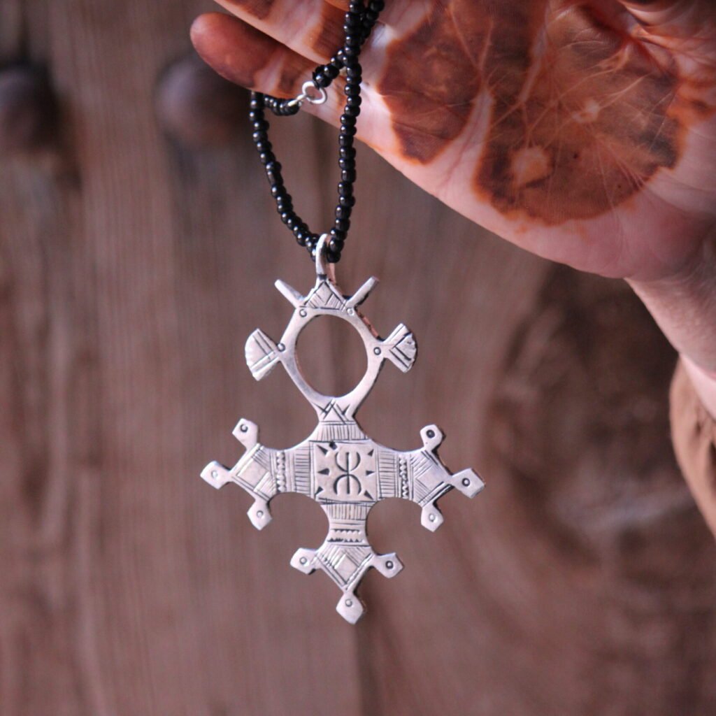 Pendentif amazigh en métal plaqué argent avec motif gravé, monté sur un collier de perles noires.