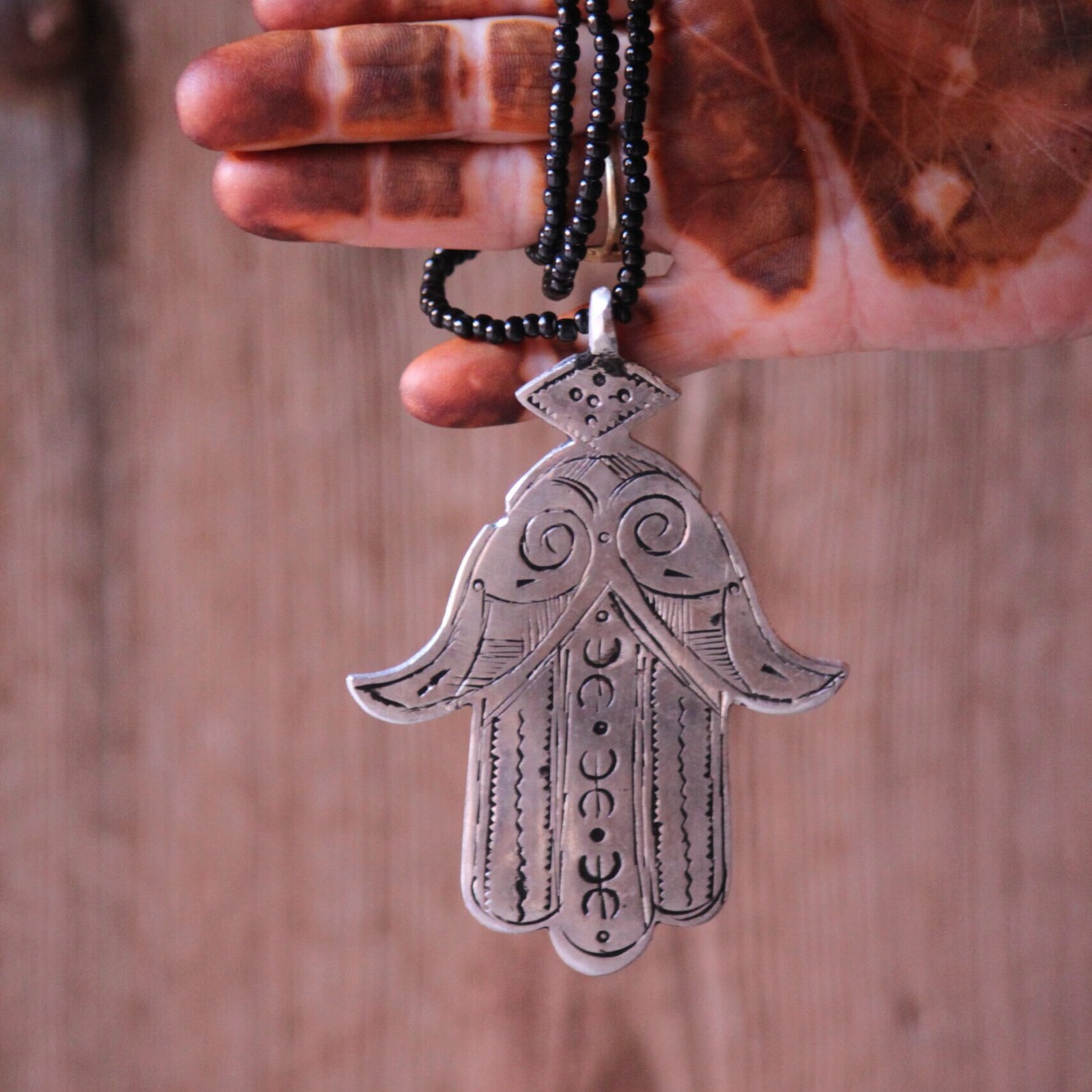 Pendentif amazigh en métal plaqué argent avec motif gravé, monté sur un collier de perles noires.