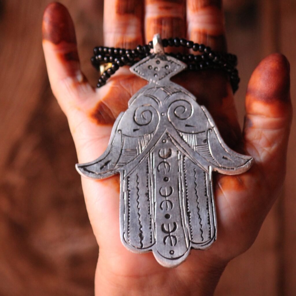 Pendentif amazigh en métal plaqué argent avec motif gravé, monté sur un collier de perles noires.