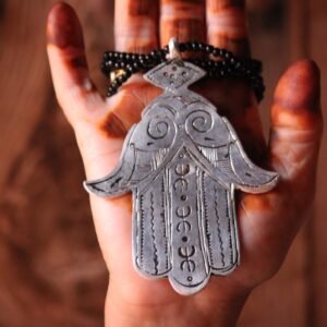 Pendentif amazigh en métal plaqué argent avec motif gravé, monté sur un collier de perles noires.