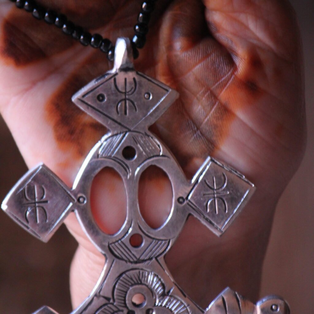 Pendentif amazigh en métal plaqué argent avec motif gravé, monté sur un collier de perles noires.