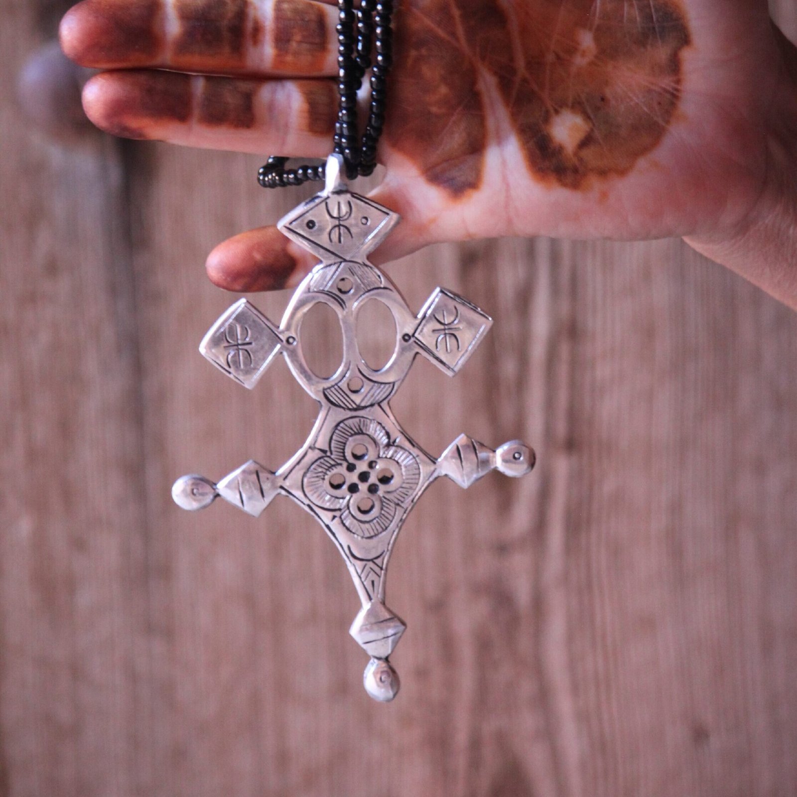 Pendentif amazigh en métal plaqué argent avec motif gravé, monté sur un collier de perles noires.