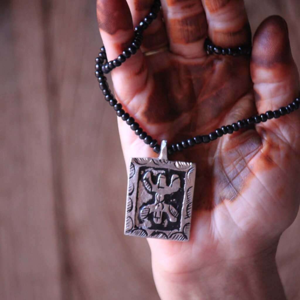 Pendentif amazigh en métal plaqué argent avec motif gravé, monté sur un collier de perles noires.