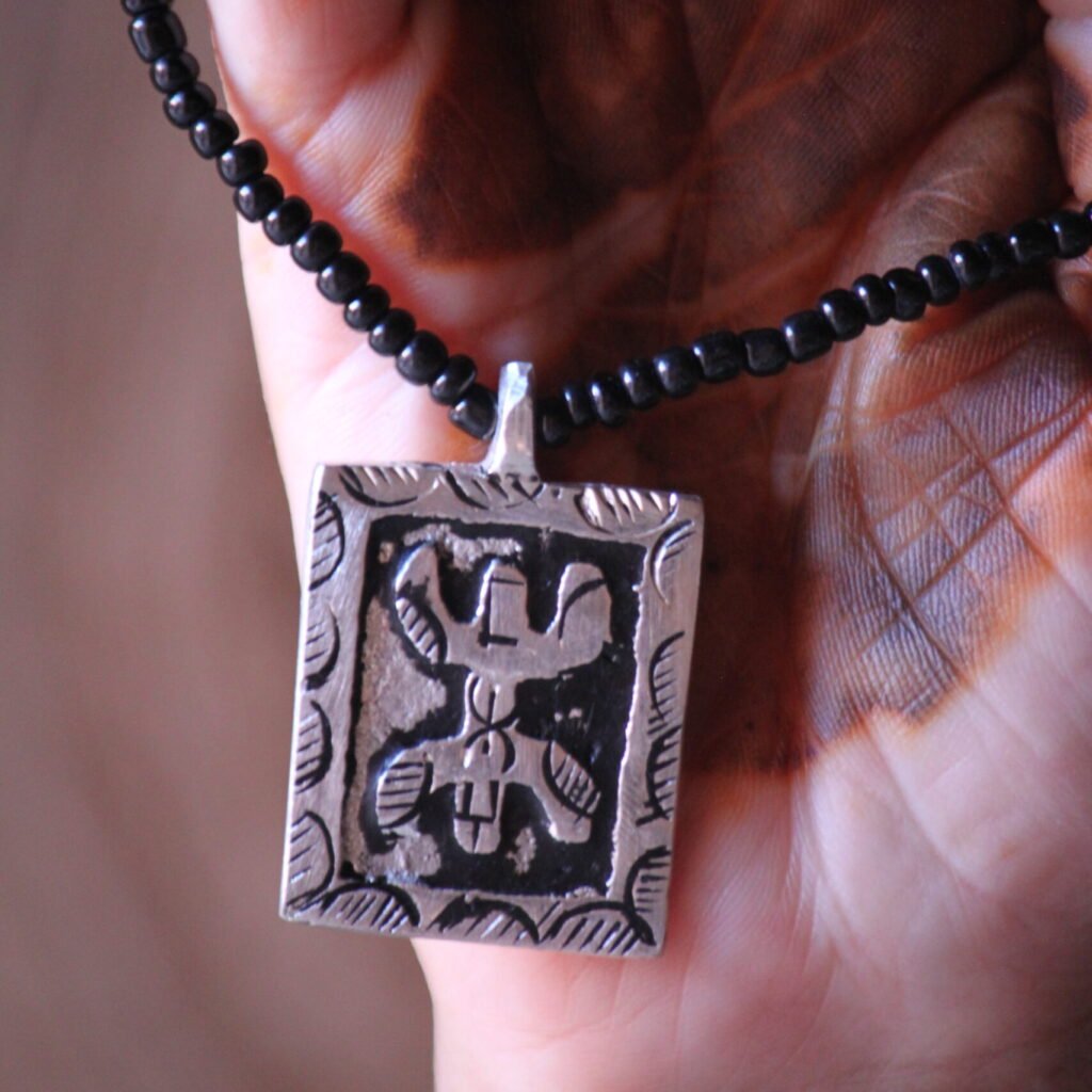 Pendentif amazigh en métal plaqué argent avec motif gravé, monté sur un collier de perles noires.