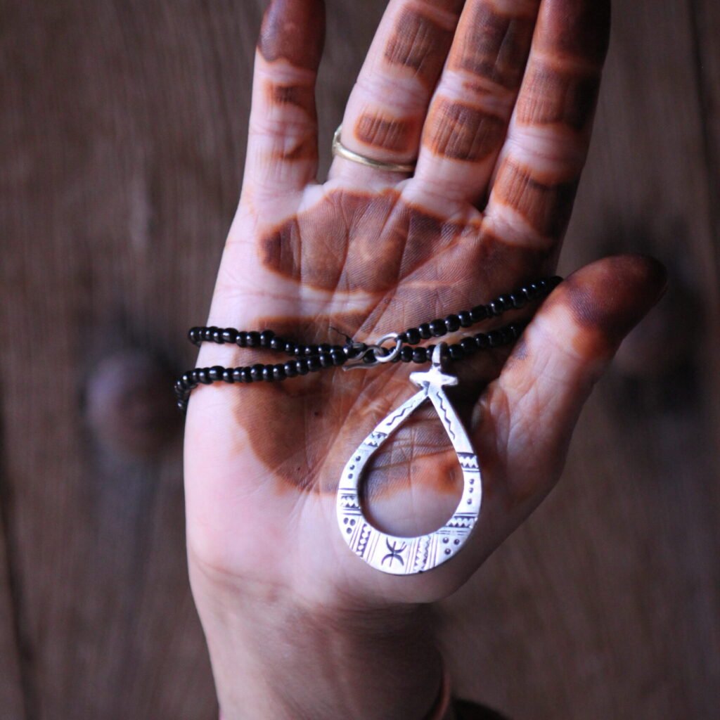 Pendentif amazigh en métal plaqué argent avec motif gravé, monté sur un collier de perles noires.