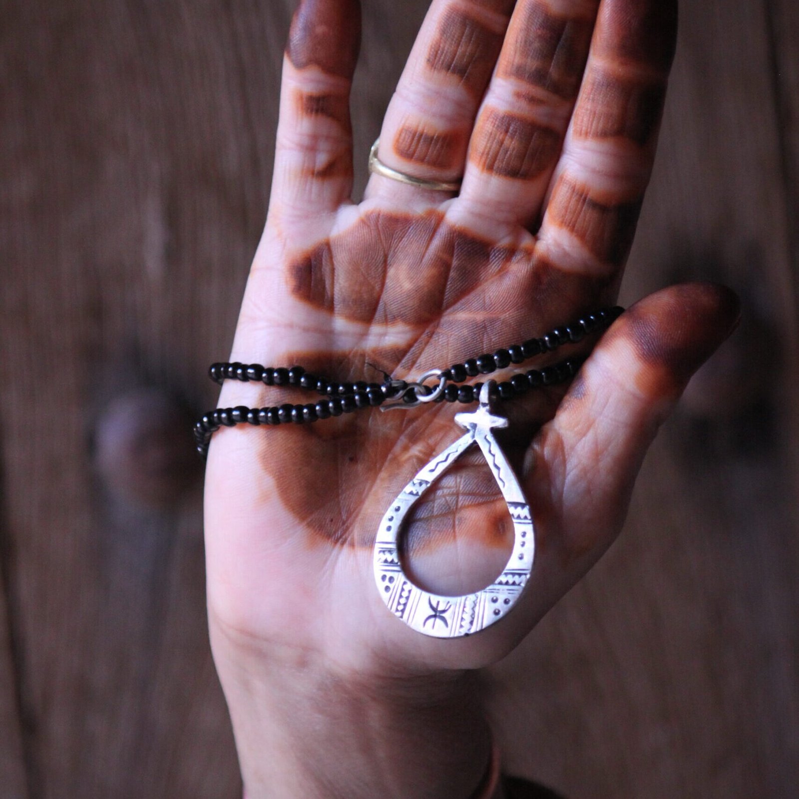 Pendentif amazigh en métal plaqué argent avec motif gravé, monté sur un collier de perles noires.
