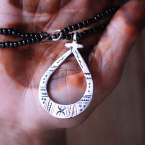 Pendentif amazigh en métal plaqué argent avec motif gravé, monté sur un collier de perles noires.