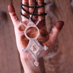 Pendentif amazigh en métal plaqué argent avec motif gravé, monté sur un collier de perles noires.