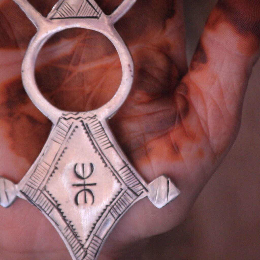 Pendentif amazigh en métal plaqué argent avec motif gravé, monté sur un collier de perles noires.