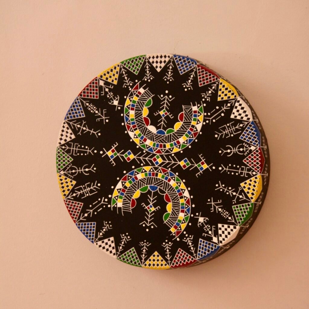Bendir peint à la main par Muha Tawargit, décoré de motifs amazighs noirs et colorés, avec une main ornée de henné au premier plan.