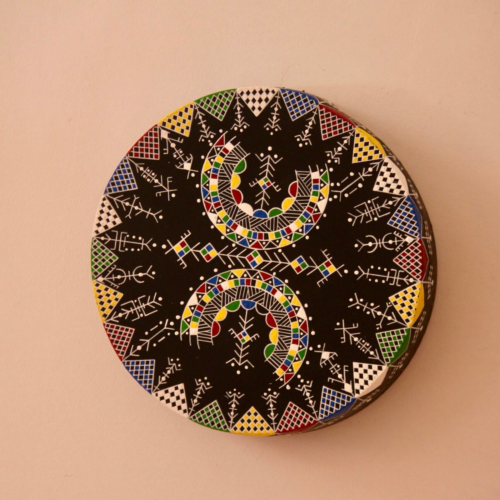 Bendir peint à la main par Muha Tawargit, décoré de motifs amazighs noirs et colorés, avec une main ornée de henné au premier plan.