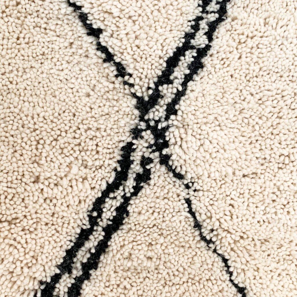 Tapis artisanal écru conçu par Afusart, tissé à la main par Malika, avec motifs amazighs noirs et touches colorées.