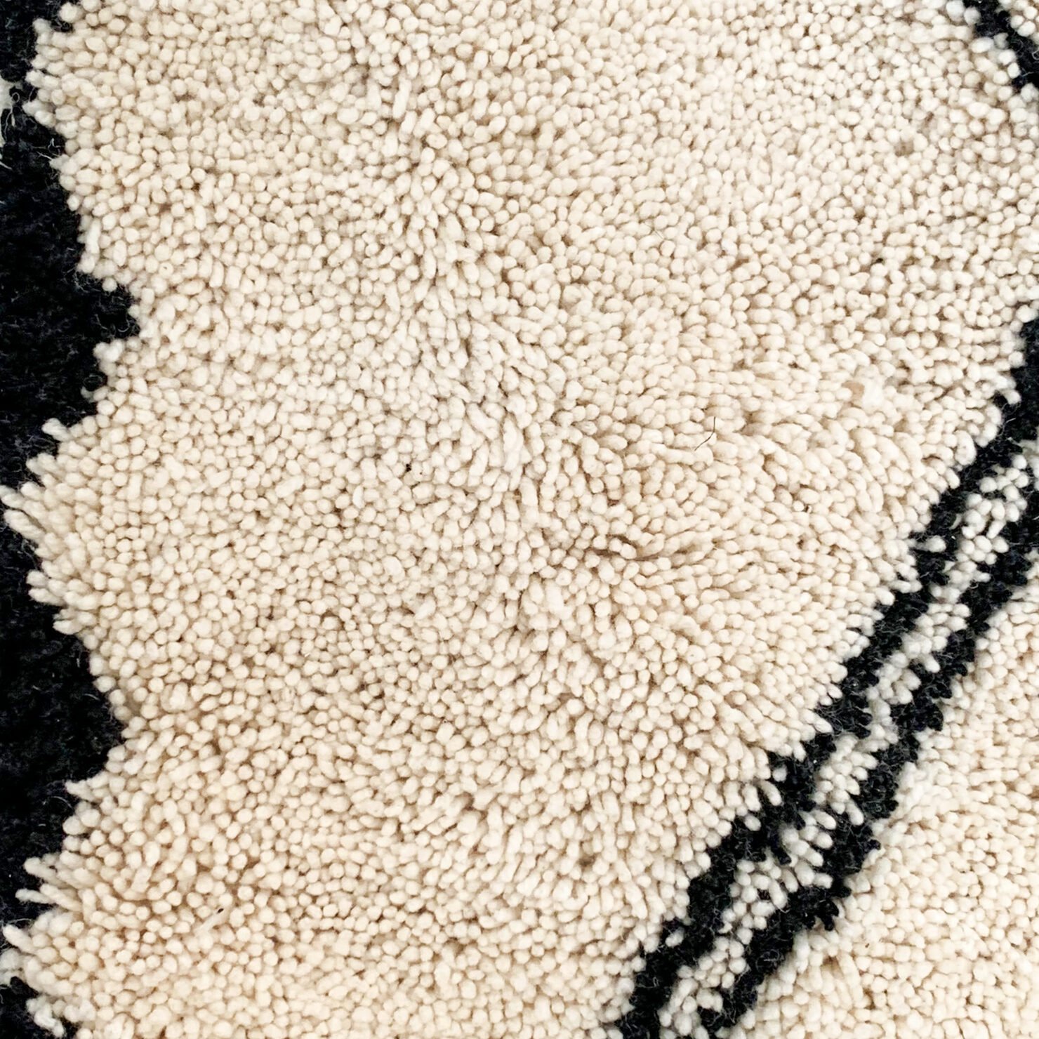 Tapis artisanal écru conçu par Afusart, tissé à la main par Malika, avec motifs amazighs noirs et touches colorées.