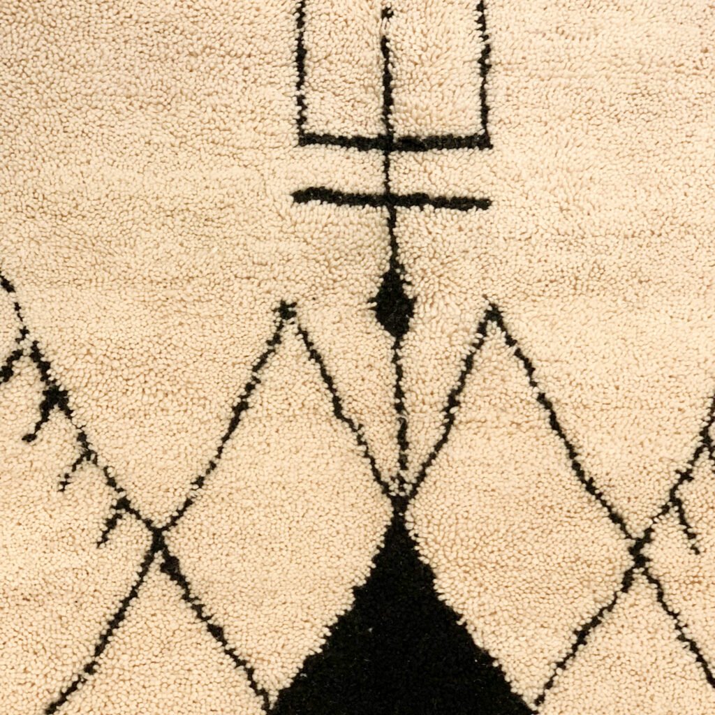 Tapis artisanal écru conçu par Afusart, tissé à la main par Malika, avec motifs amazighs noirs et touches colorées.