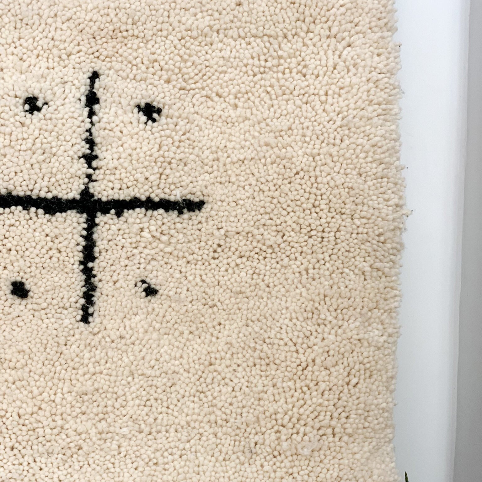 Tapis artisanal écru conçu par Afusart, tissé à la main par Malika, avec motifs amazighs noirs et touches colorées.