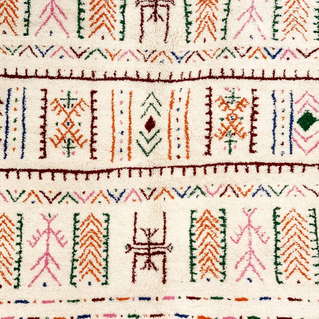 Tapis artisanal écru conçu par Afusart, tissé à la main par Malika, avec motifs amazighs noirs et touches colorées.