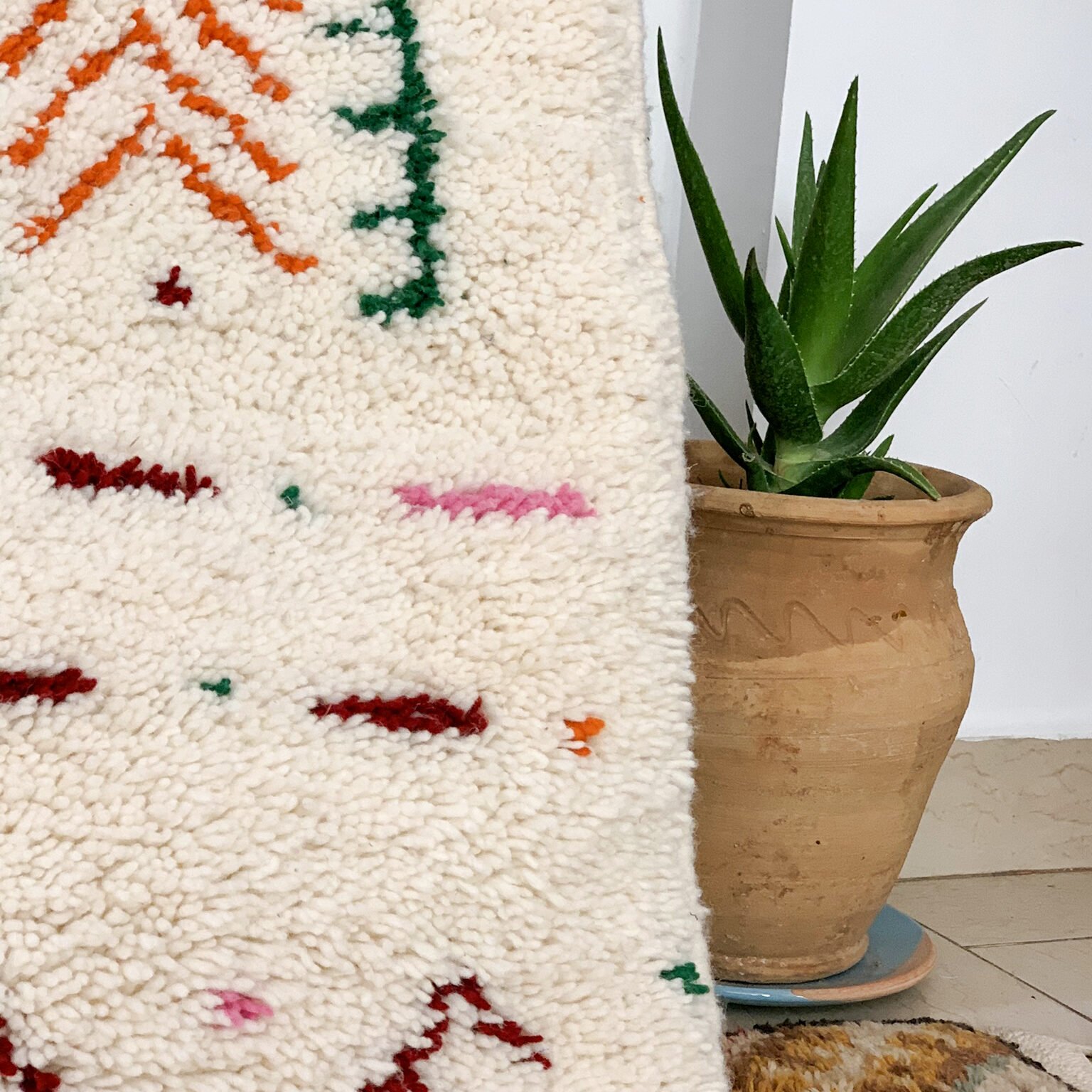 Tapis artisanal écru conçu par Afusart, tissé à la main par Malika, avec motifs amazighs noirs et touches colorées.