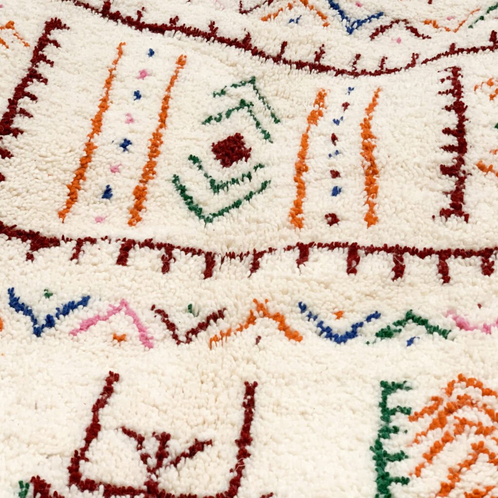 Tapis artisanal écru conçu par Afusart, tissé à la main par Malika, avec motifs amazighs noirs et touches colorées.