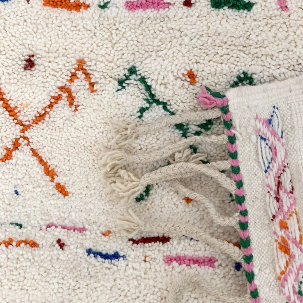 Tapis artisanal écru conçu par Afusart, tissé à la main par Malika, avec motifs amazighs noirs et touches colorées.