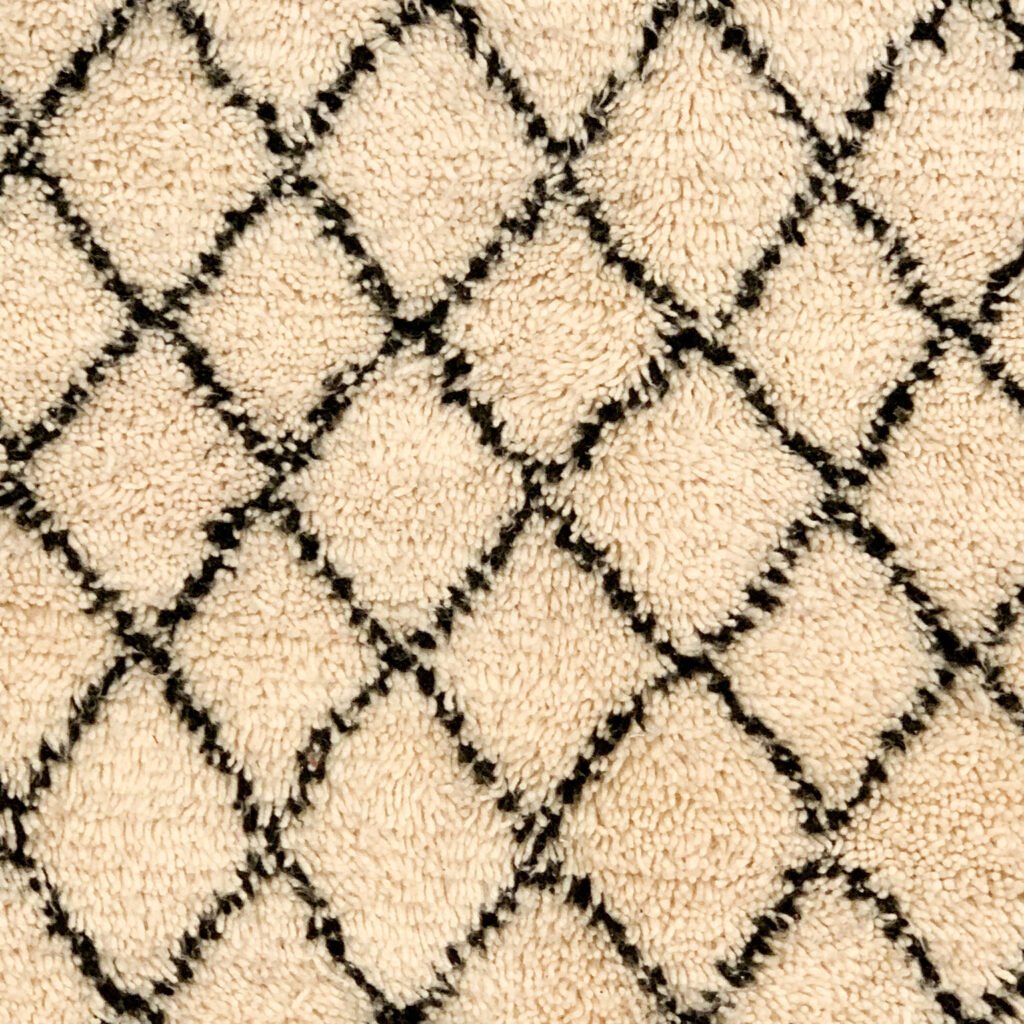 Tapis artisanal écru conçu par Afusart, tissé à la main par Malika, avec motifs amazighs noirs et touches colorées.