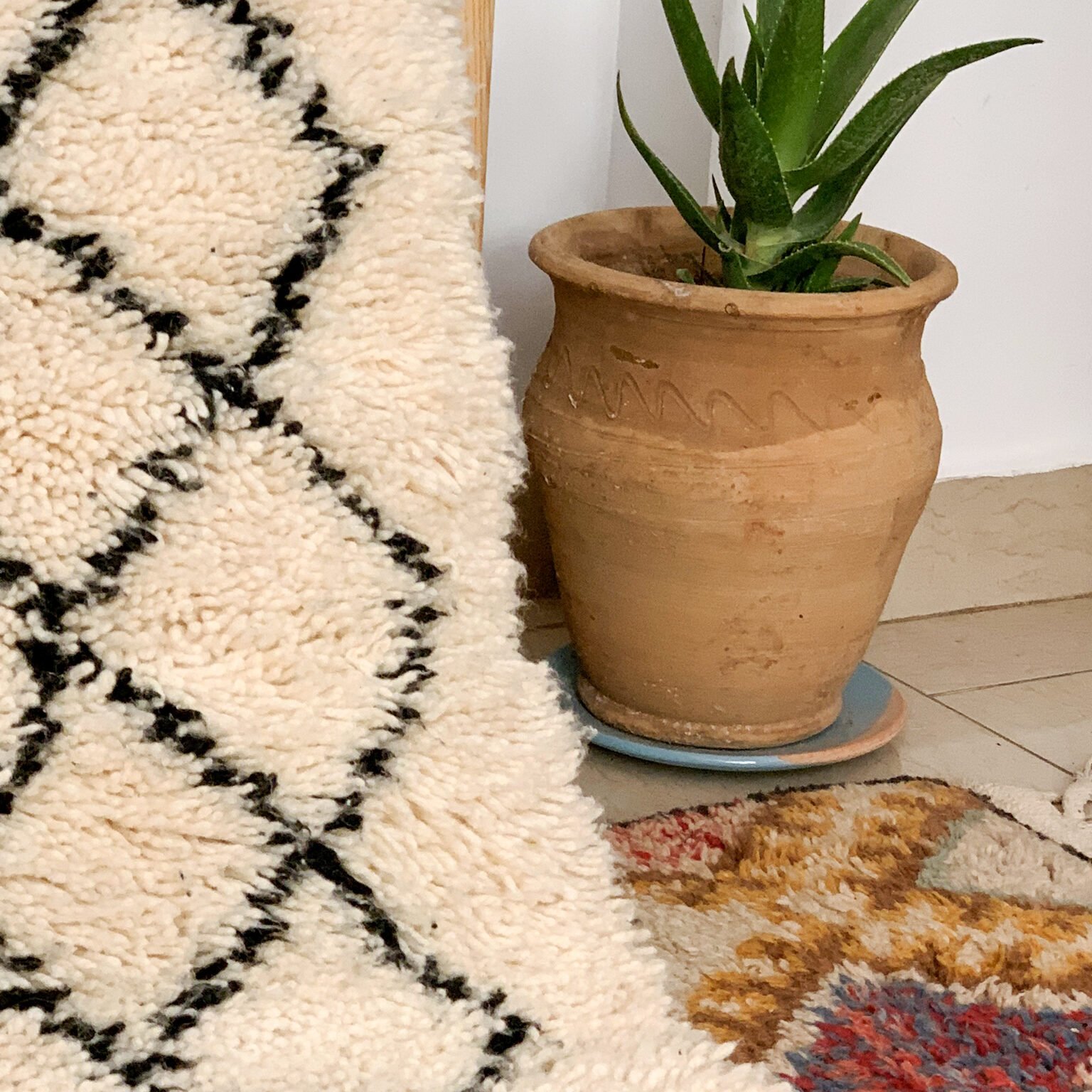 Tapis artisanal écru conçu par Afusart, tissé à la main par Malika, avec motifs amazighs noirs et touches colorées.
