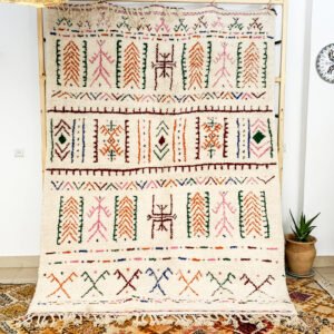 Tapis artisanal écru conçu par Afusart, tissé à la main par Malika, avec motifs amazighs noirs et touches colorées.