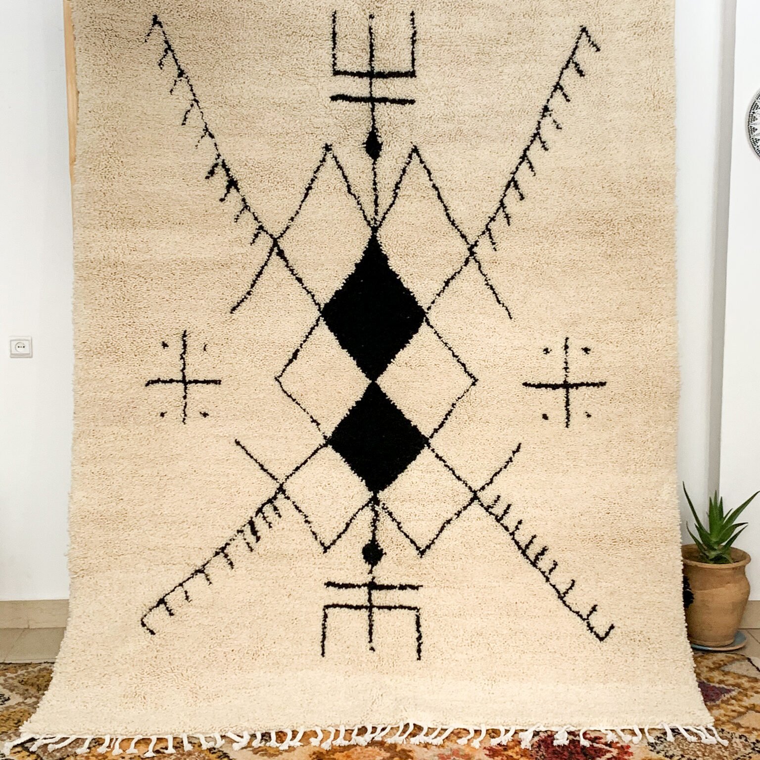 Tapis artisanal écru conçu par Afusart, tissé à la main par Malika, avec motifs amazighs noirs et touches colorées.