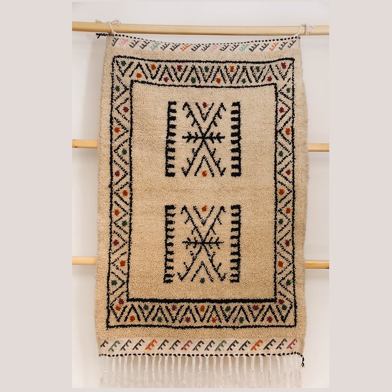 Tapis artisanal écru conçu par Afusart, tissé à la main par Malika, avec motifs amazighs noirs et touches colorées.