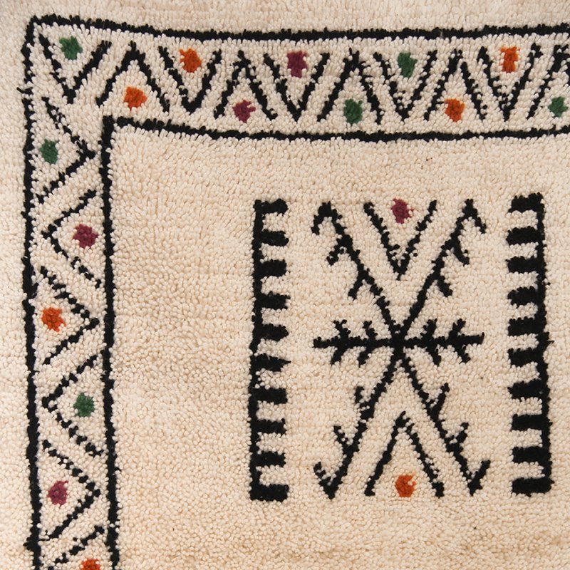 Tapis artisanal écru conçu par Afusart, tissé à la main par Malika, avec motifs amazighs noirs et touches colorées.