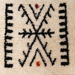 Tapis artisanal écru conçu par Afusart, tissé à la main par Malika, avec motifs amazighs noirs et touches colorées.